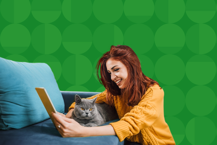 Young woman looking at her tablet while hugging her cat laying on the couch