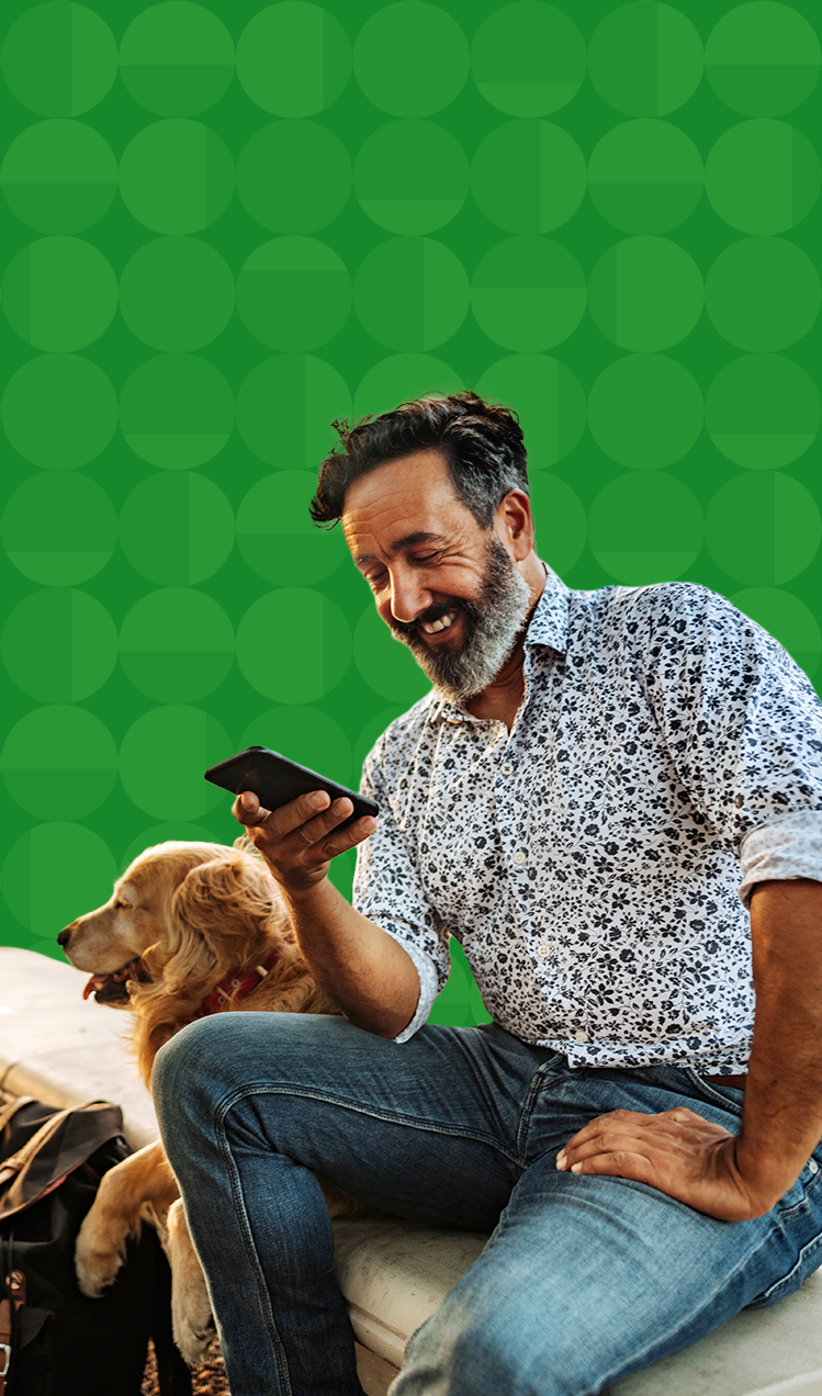 Man and his dog sitting outdoors while he looks at his phone