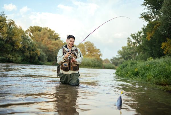 Man standing in the water and pulls out the fish that he caught with a satisfactory smile on his face
