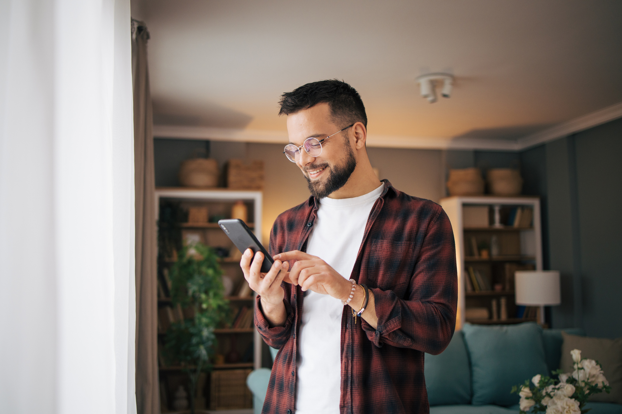 Happy adult man standing in front of the window looking at his phone