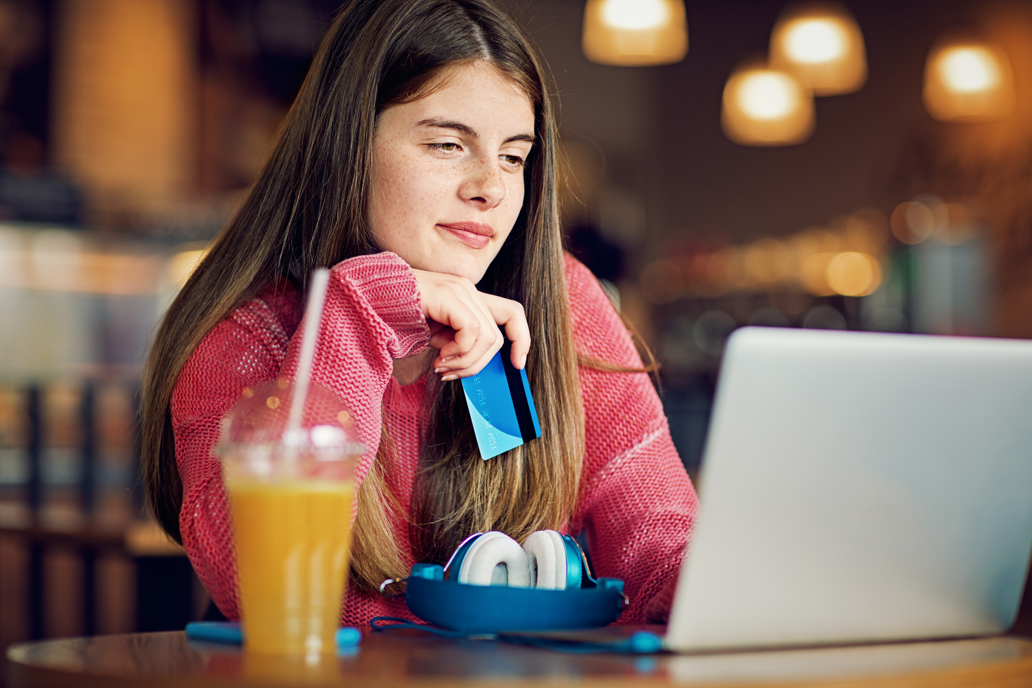 Teenage girl sitting at a cafe with her card in hand online shopping on her laptop