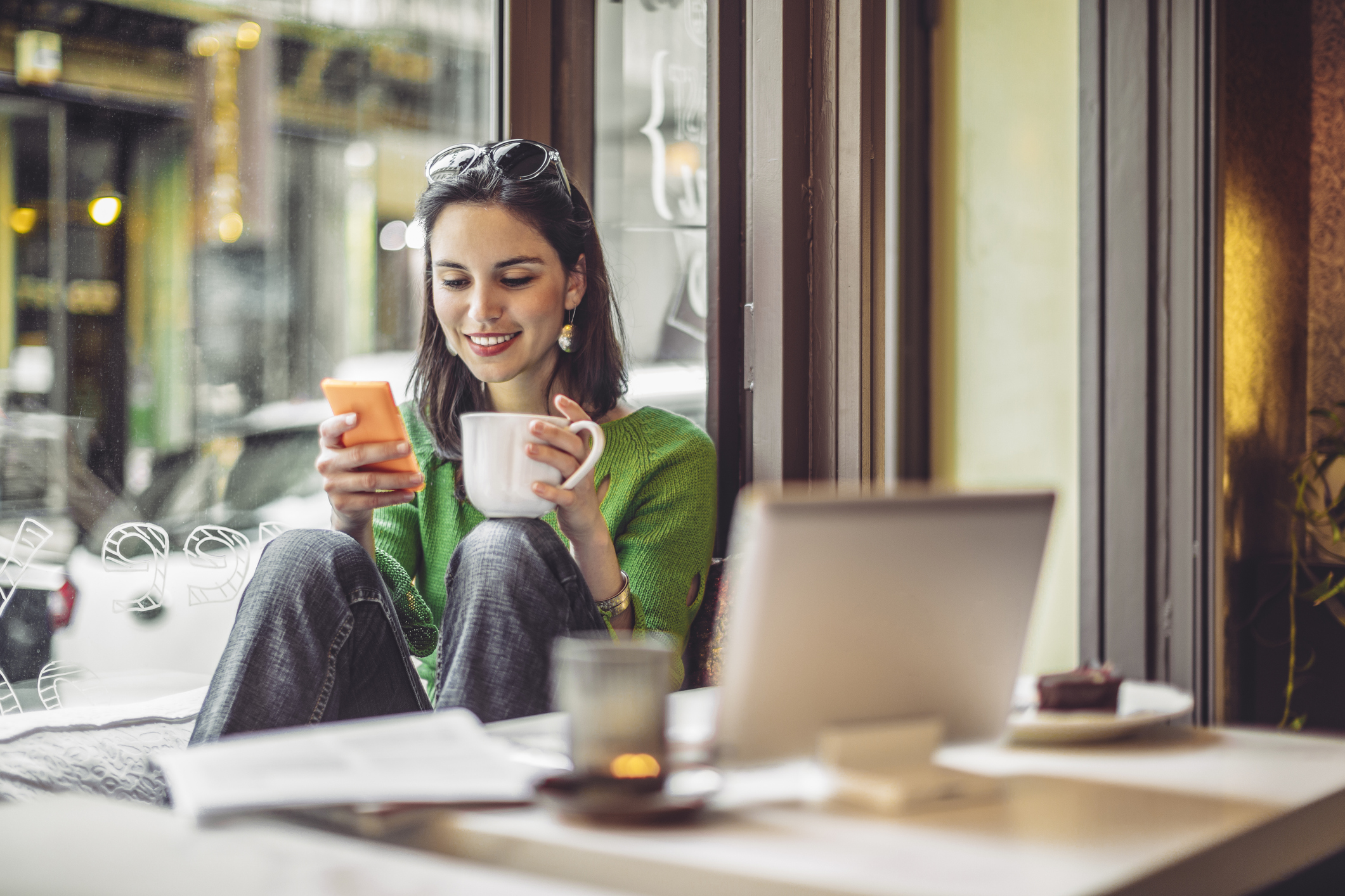 Young woman enjoying a cup of coffee at a cafe while looking at her phone