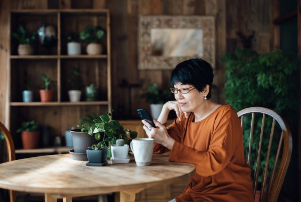 Image: Older Asian woman sitting at kitchen table with her mobile phone.