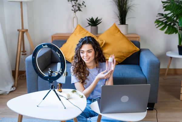 Image: Curly-haired woman showcasing skincare products on camera.