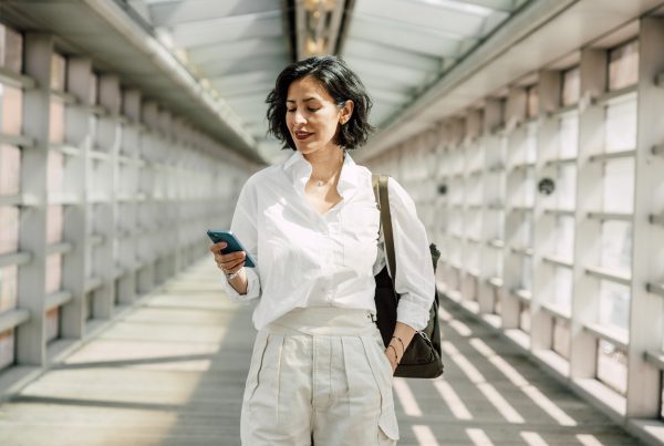 Image: Woman in business dress walking and using phone.