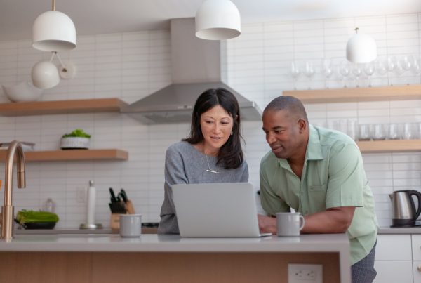 Husband and wife in their kitchen using a laptop computer to pay bills online and manage their budget.
