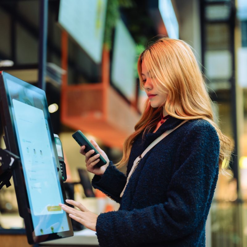 Woman at cashier counter uses smartphone for payment..