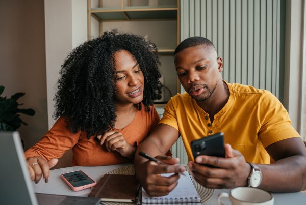 Couple sitting at table together with phones, laptop, and paperwork filing taxes.