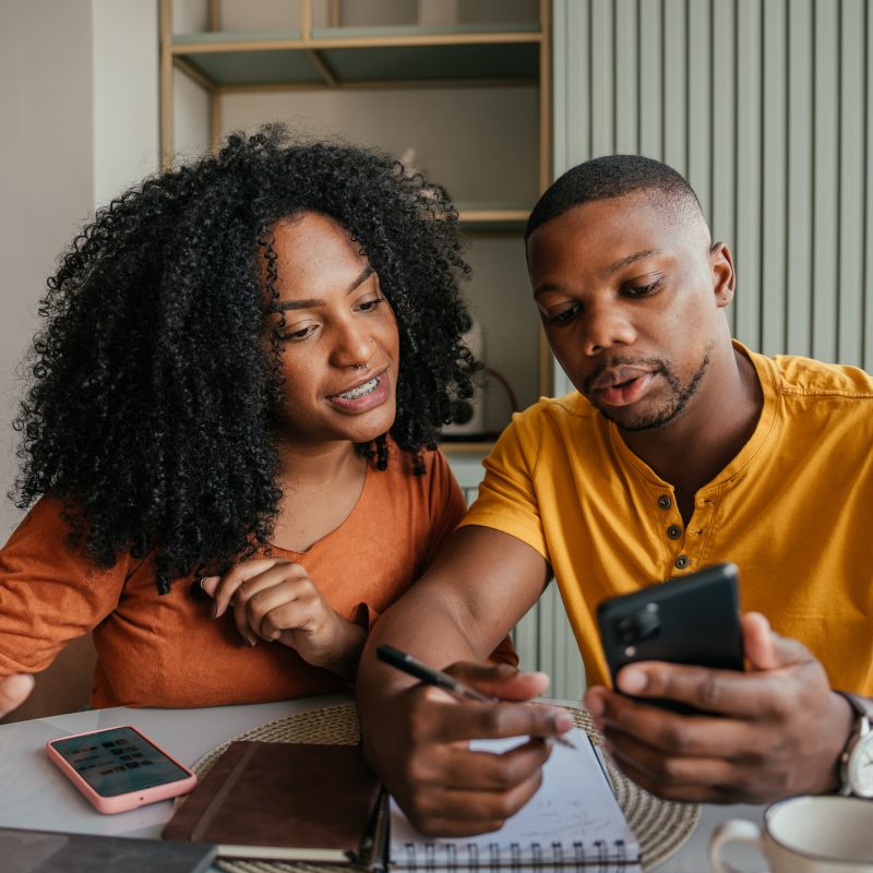 Couple sitting at table together with phones, laptop, and paperwork filing taxes.