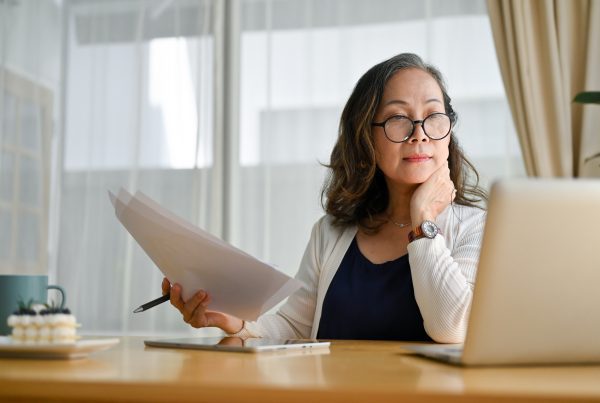 Concentrated middle aged woman using portable computer and examining paperwork.