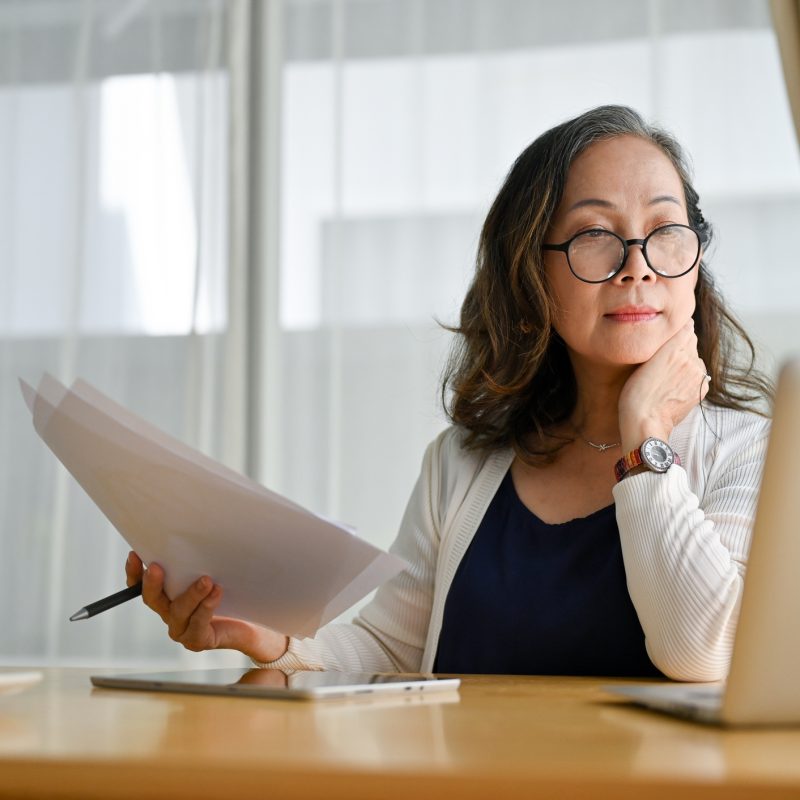 Concentrated middle aged woman using portable computer and examining paperwork.