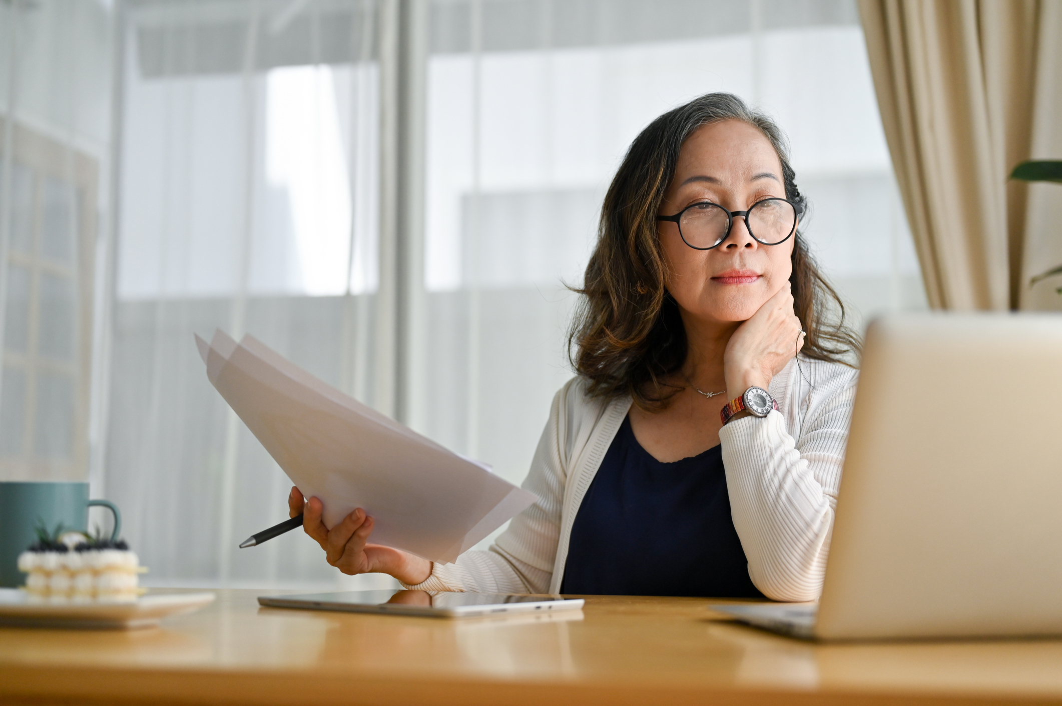Concentrated middle aged woman using portable computer and examining paperwork.