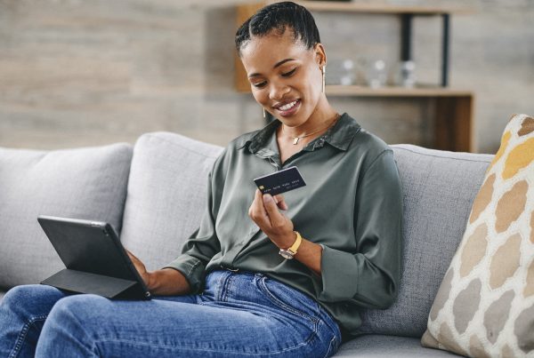 Woman holding credit card and shopping online with digital tablet on sofa at home.