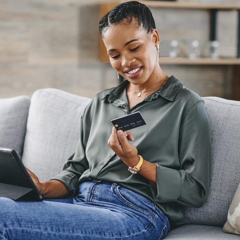 Woman holding credit card and shopping online with digital tablet on sofa at home.