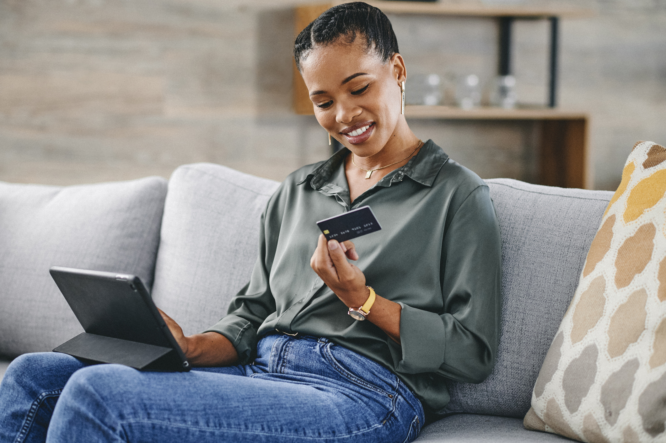 Woman holding credit card and shopping online with digital tablet on sofa at home.