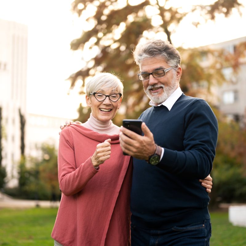 senior couple walking and using smart phone in public park