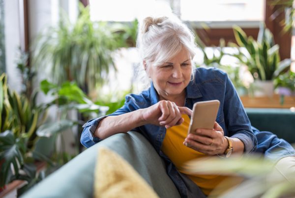Smiling senior woman using smart phone while sitting on sofa at home