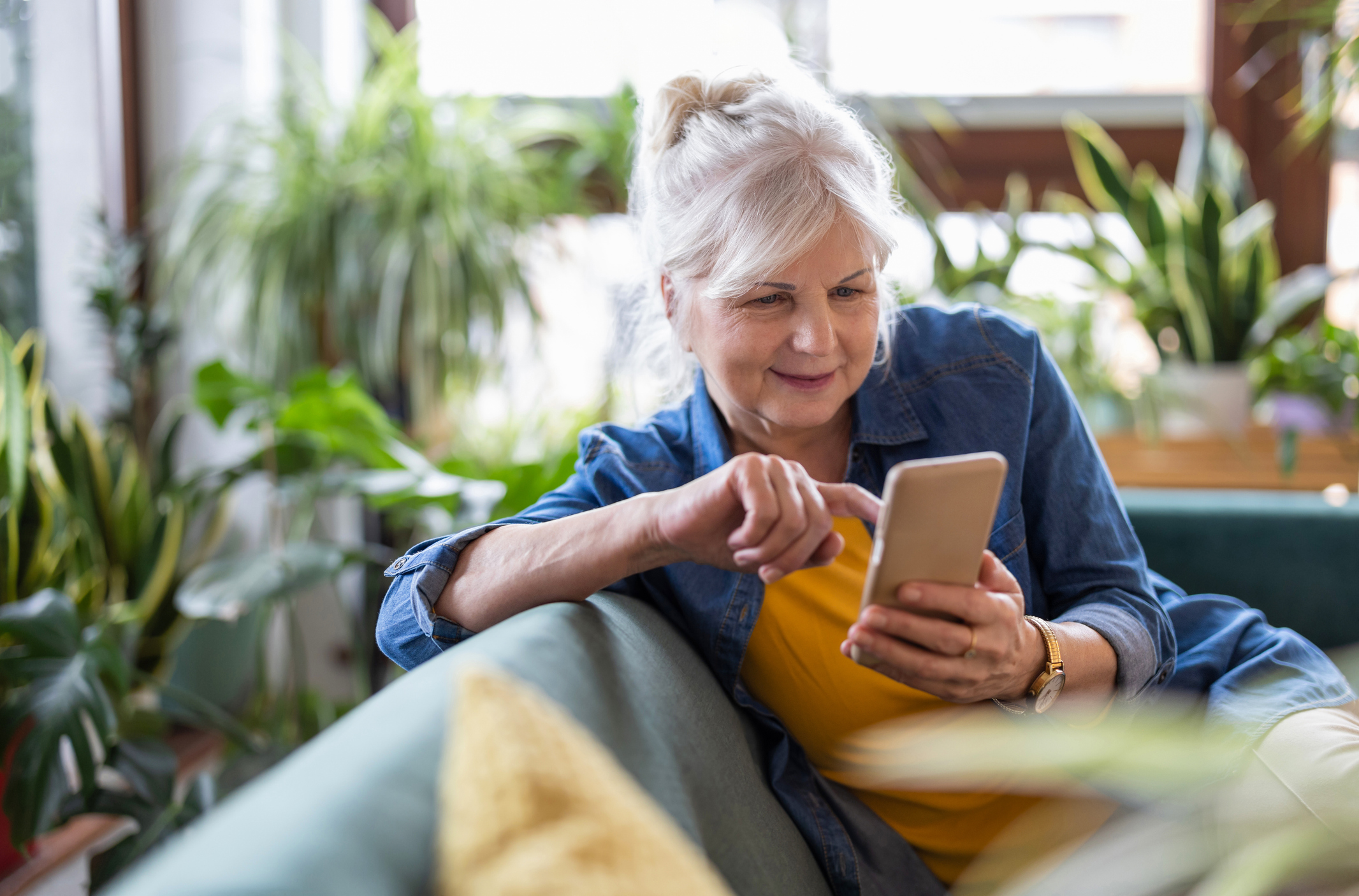Smiling senior woman using smart phone while sitting on sofa at home