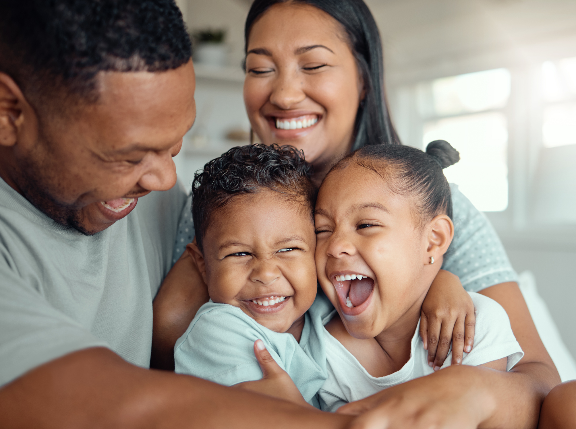 family with two children wearing pyjamas and sitting together embracing each other at home. Cheerful parents sitting with their daughter and son laughing and having fun in the morning
