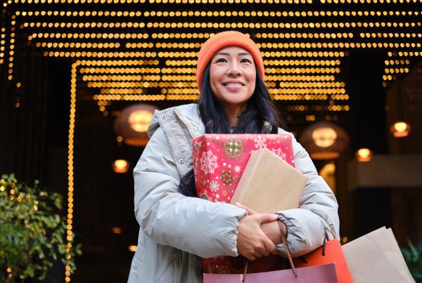 Smiling young woman carrying christmas gifts and shopping bags in a decorated street