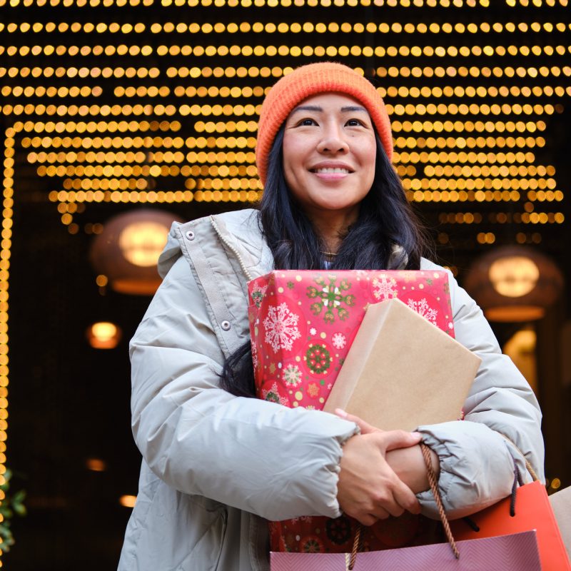 Smiling young woman carrying christmas gifts and shopping bags in a decorated street