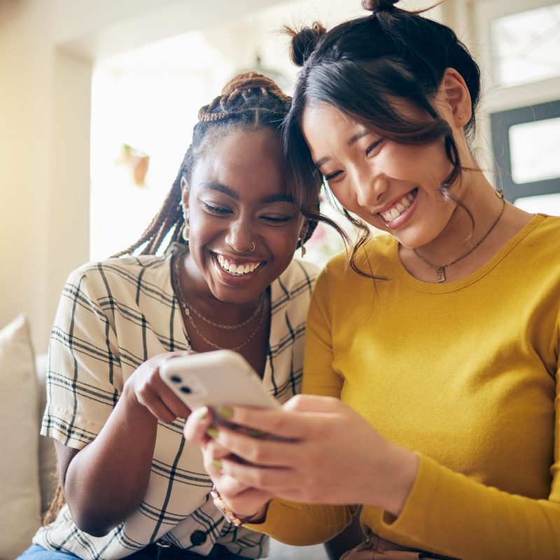 Young women, funny meme and smartphone, friends relax at home with social media and communication. Gen z, happiness and comedy online, chat and using phone with people on couch, mobile app and tech